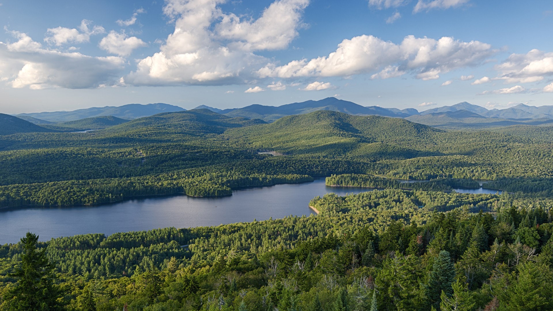 Aerial view of the Adirondack Mountains with a lake surrounded by dense forest in New York State